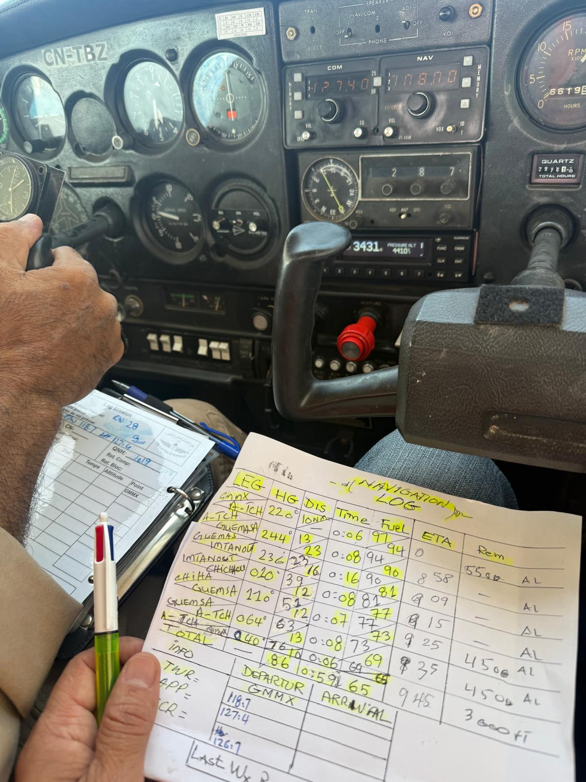 Intérieur du cockpit du CN-TBZ, un carnet de navigation tenu à la main devant le tableau de bord